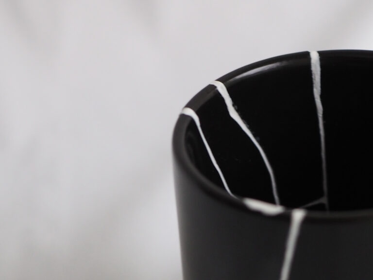 黒い陶器カップの縁に施された白いモダン金継ぎ(白継ぎ)の修復跡アップ
