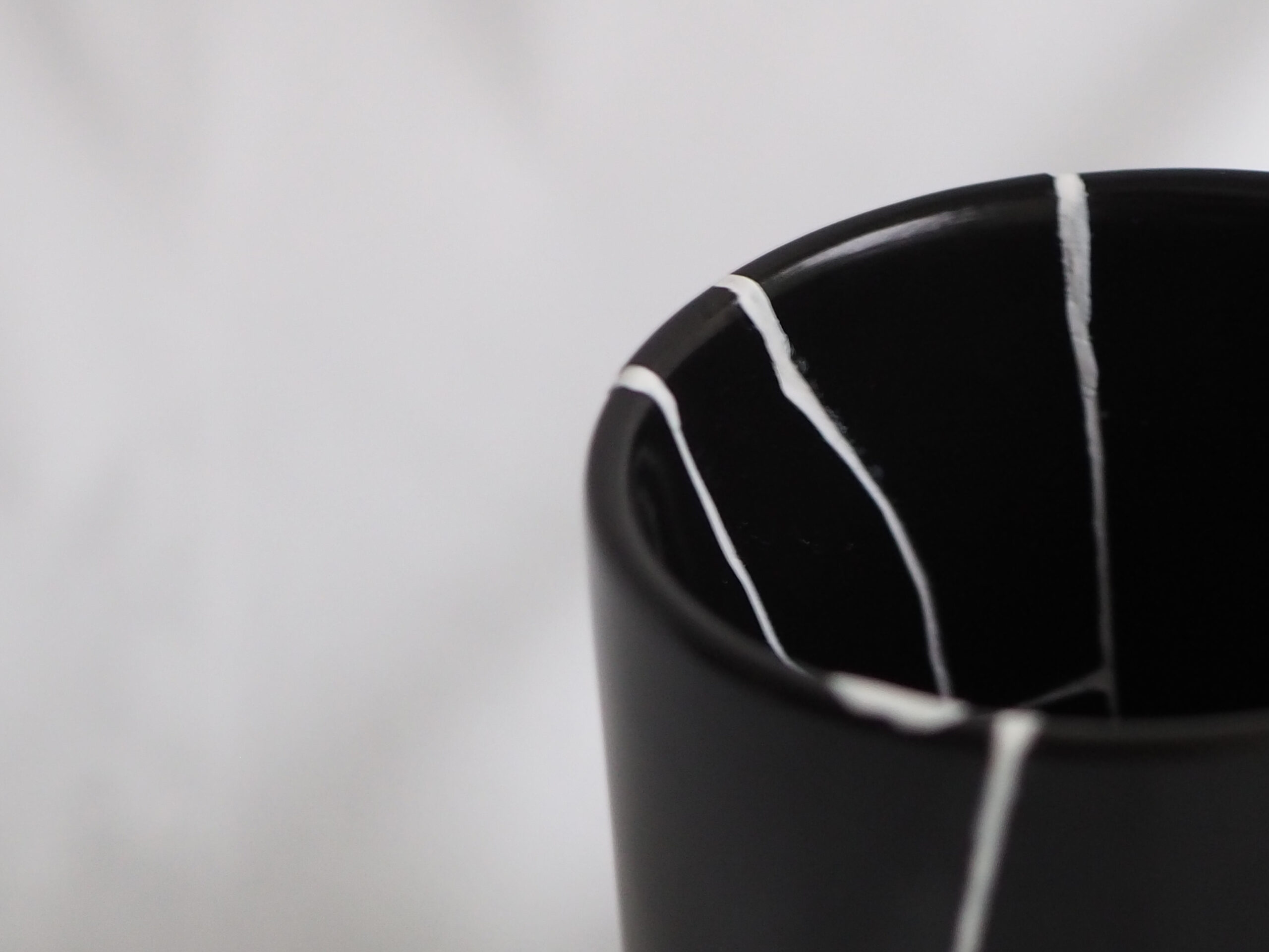 黒い陶器カップの縁に施された白いモダン金継ぎ（白継ぎ）の修復跡アップ